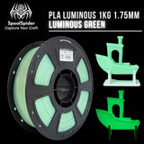 A spool of PLA luminous 1KG 1.75mm filament in luminous green, shown alongside 3D boat models demonstrating its glow-in-the-dark effect, on a black background with the brand SpoolSpider.